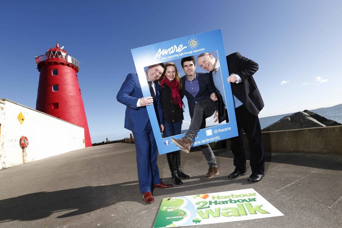 Group posing with Aware event frame by a red lighthouse, promoting Harbour 2 Harbour Walk.