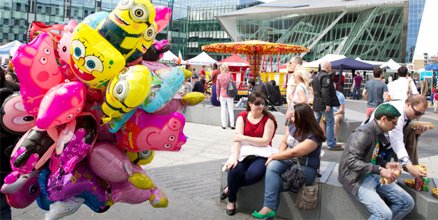 Colorful balloons and people enjoying a lively outdoor market scene on a sunny day.