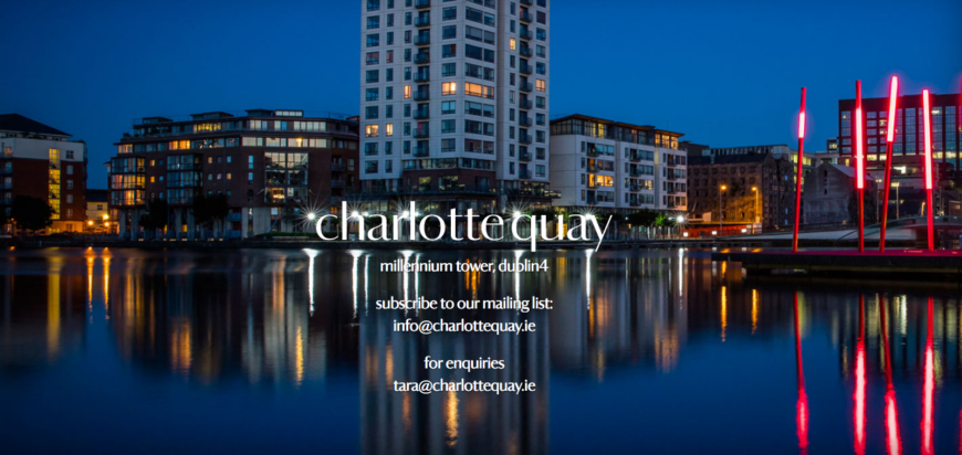 Charlotte Quay Dublin night view with buildings and illuminated red poles reflecting on calm water.