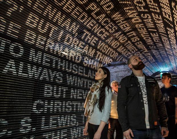 People exploring an illuminated tunnel displaying text on walls, creating an immersive experience.