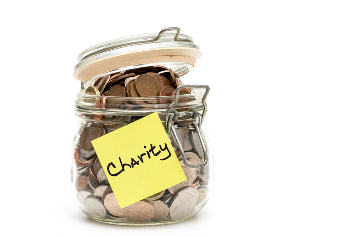 Glass jar filled with coins, labeled Charity on a sticky note, symbolizing donations and generosity.