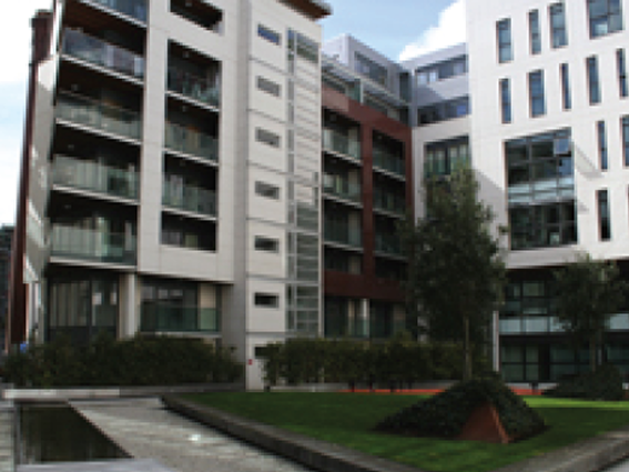 Modern apartment complex with courtyard, featuring greenery and sleek architectural design under a clear sky.