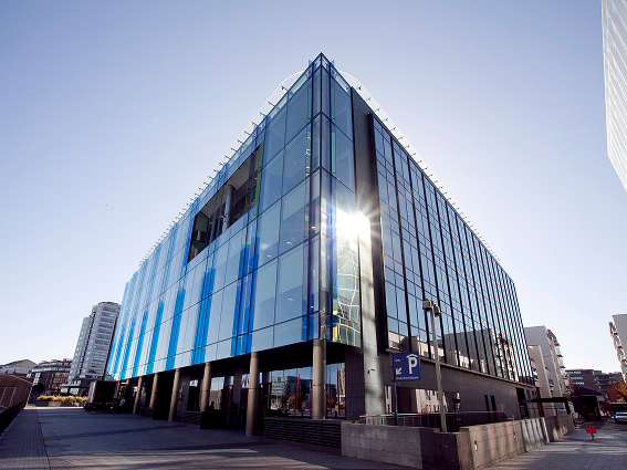 Modern glass office building with sun reflection, clear sky, and urban surroundings.