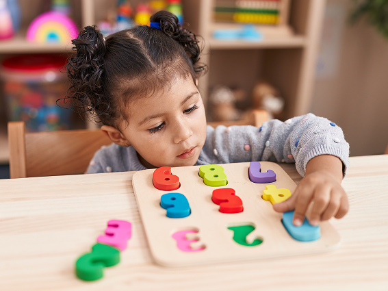 Toddler engaged with colorful number puzzle at wooden table in a playroom.