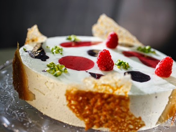 Elegant raspberry mousse cake with decorative toppings of pistachios and caramel garnish on a glass platter.