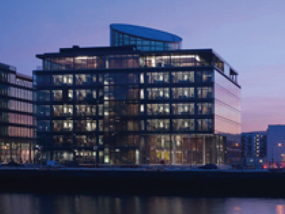 Modern glass office building illuminated at dusk by the waterfront, reflecting in the water.