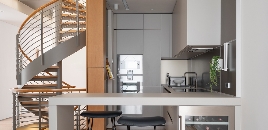 Modern kitchen with sleek cabinetry, spiral staircase, bar seating, and built-in appliances for a minimalist design.