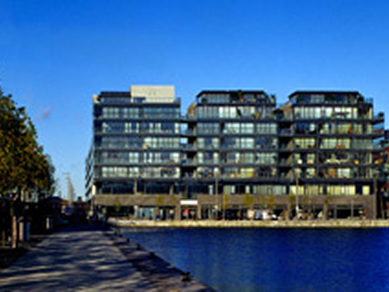Modern waterfront apartments with glass facades under a clear blue sky.