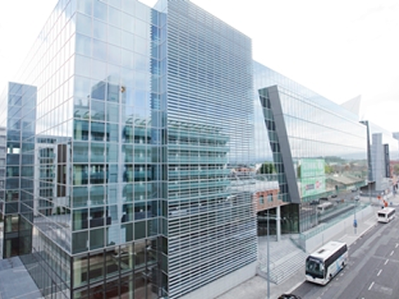 Modern glass office building with street view and bus in foreground on a clear day.