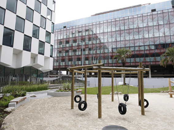 Modern office buildings next to a playground with tire swings and sand.