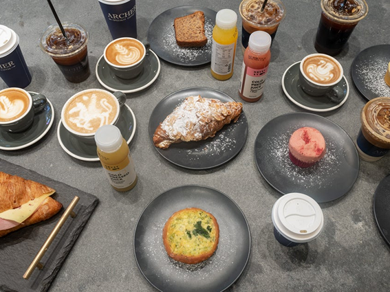 Assorted coffee drinks, pastries, and juices on a gray table at a café, ready for breakfast.