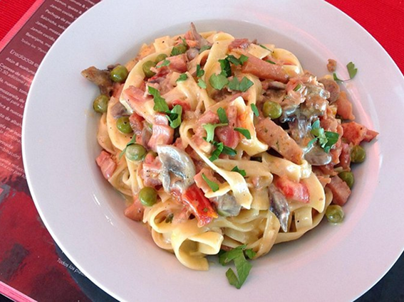 Creamy pasta primavera with mushrooms, ham, and peas garnished with fresh parsley in a white bowl.