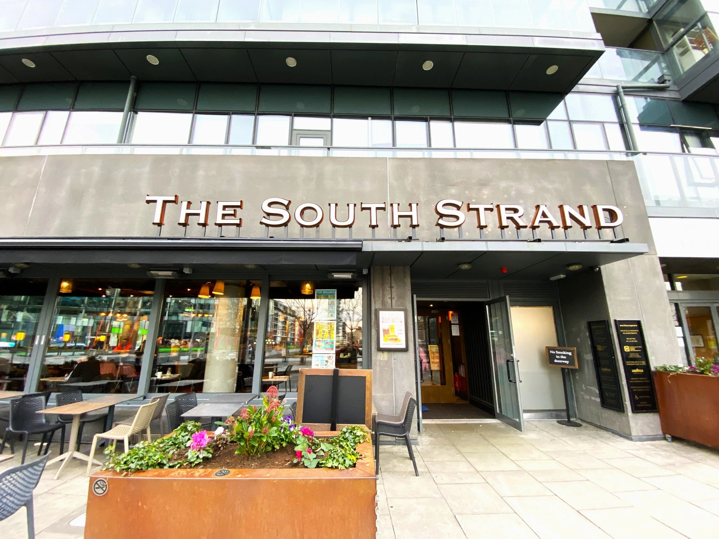 Front entrance of The South Strand restaurant with outdoor seating and signage.