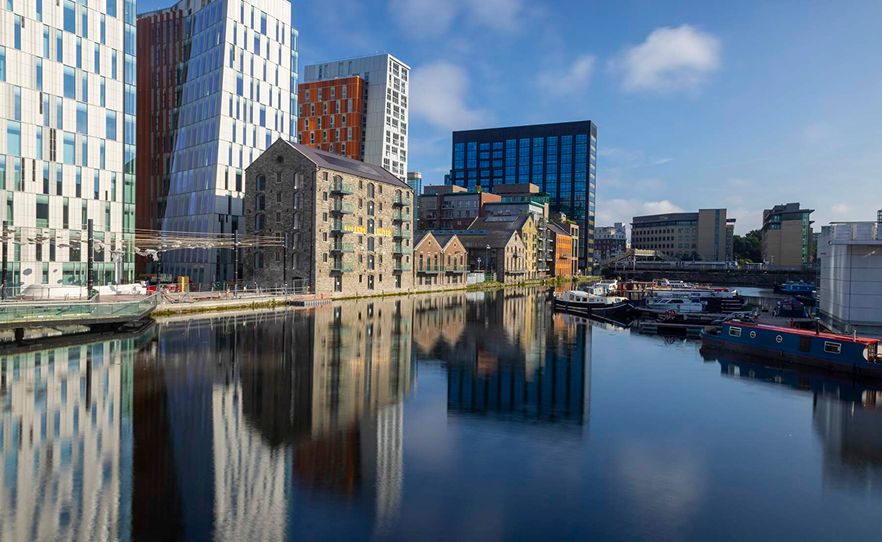 Modern buildings and historical structures reflecting in Dublin's Grand Canal Dock on a clear day.