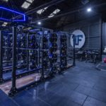 Modern gym with weightlifting equipment and neon lighting, featuring racks and colorful plates in a spacious interior.