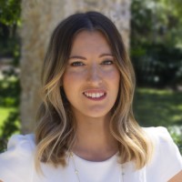 Woman wearing a simple white dress, standing and looking ahead.