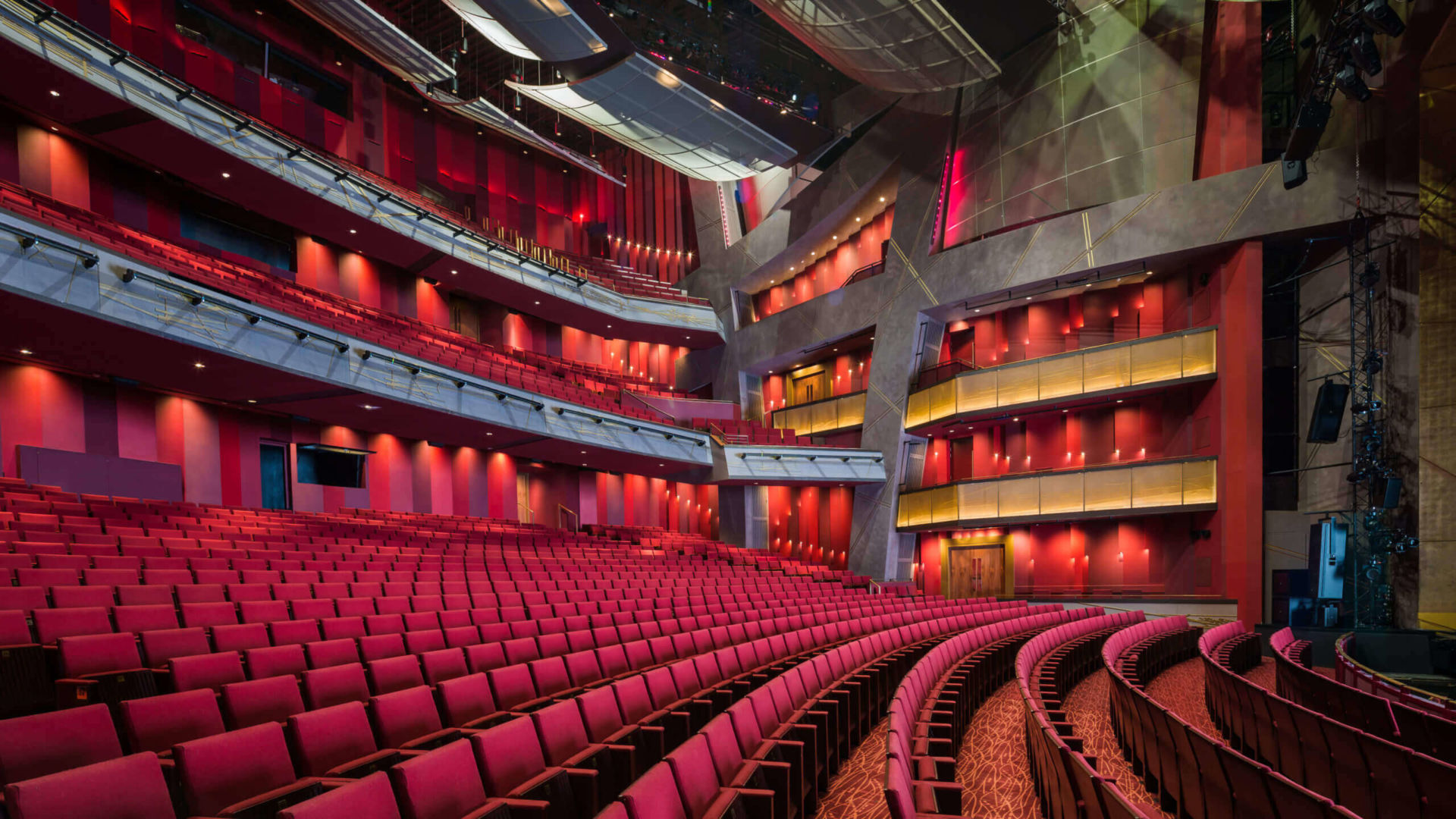 Modern theater interior with red seats and balconies, featuring dramatic lighting and architectural design.