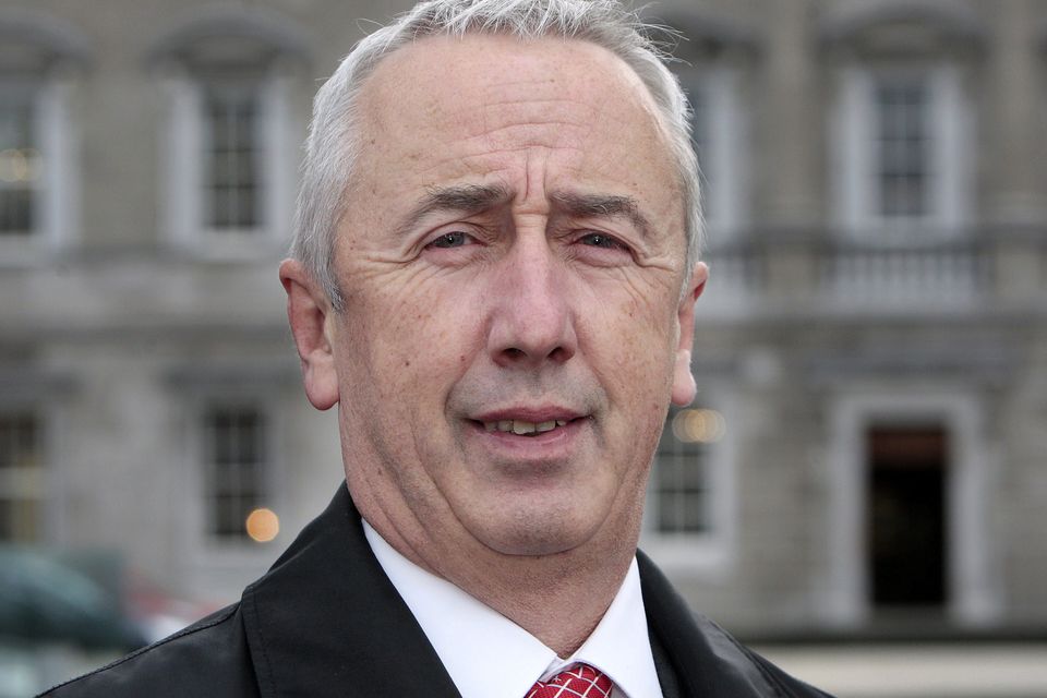 Elderly man in a suit standing outdoors in front of a historic building.