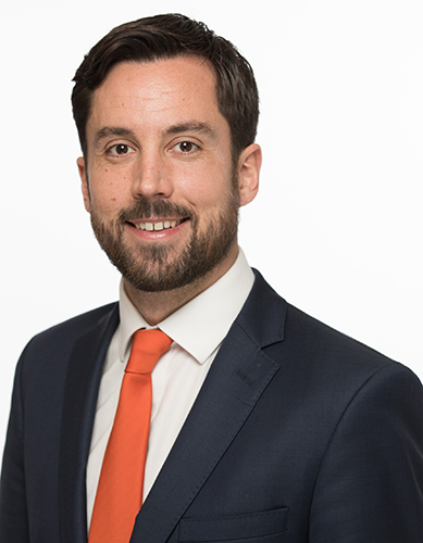 Smiling man in suit and orange tie, posing against a plain white background.