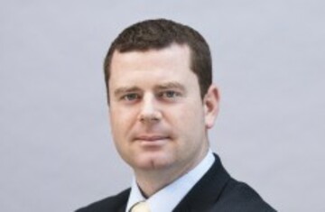 Professional man in a suit with a neutral background, looking confident and composed.