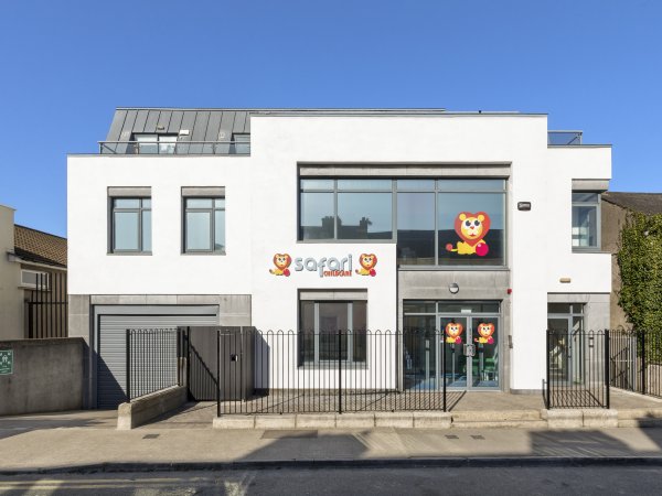 Modern white building with Safari Kids logo and lion graphics, featuring large glass windows under a clear blue sky.